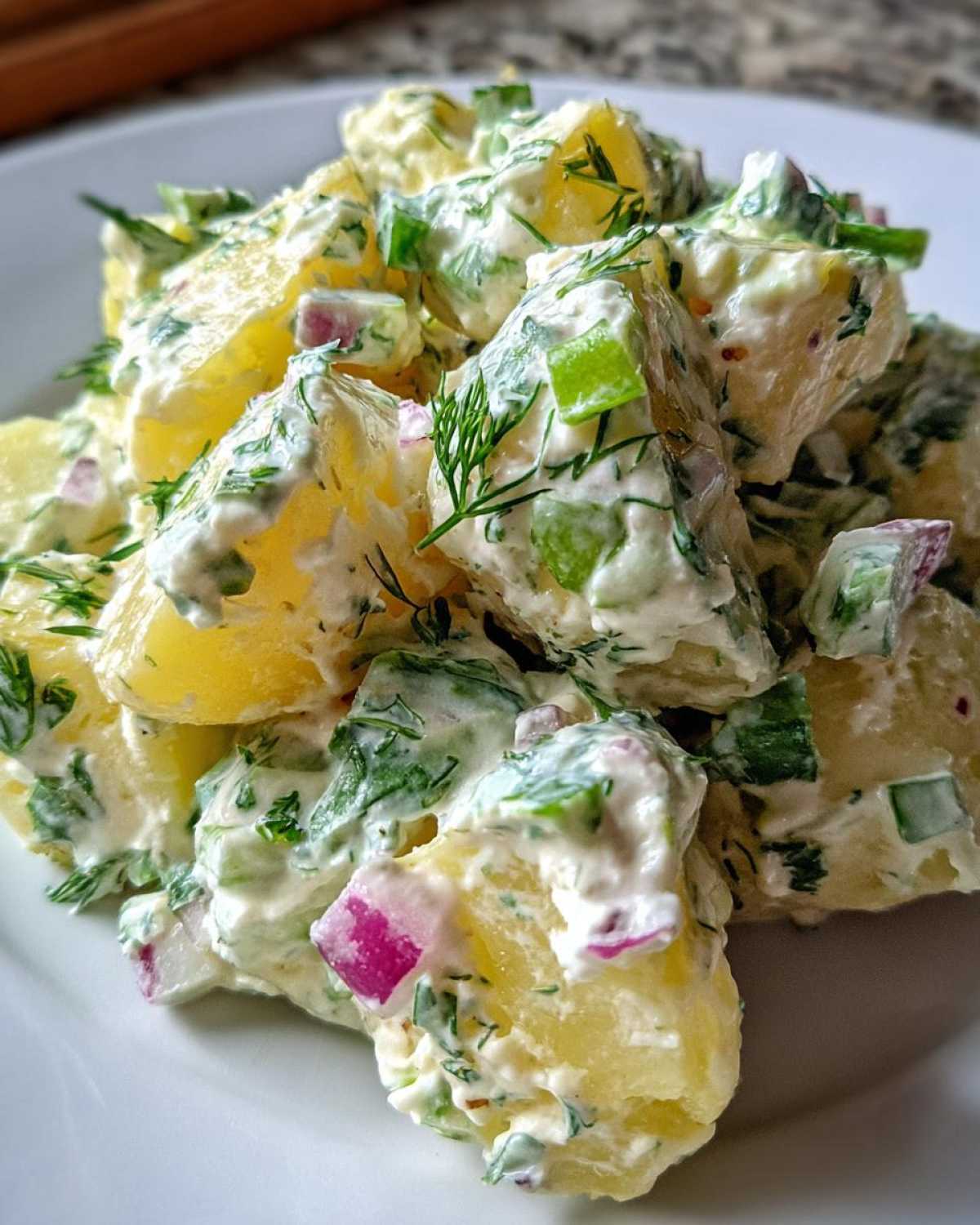 Close-up of chunks of yellow potato coated in a creamy dressing with fresh dill, red onion, and celery, showcasing the Creamy Dill Potato Salad.