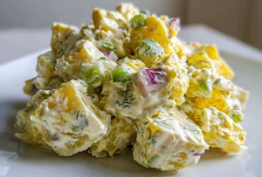 A close-up shot of a mound of Creamy Dill Potato Salad featuring yellow potatoes, red onion, green celery, and fresh dill.