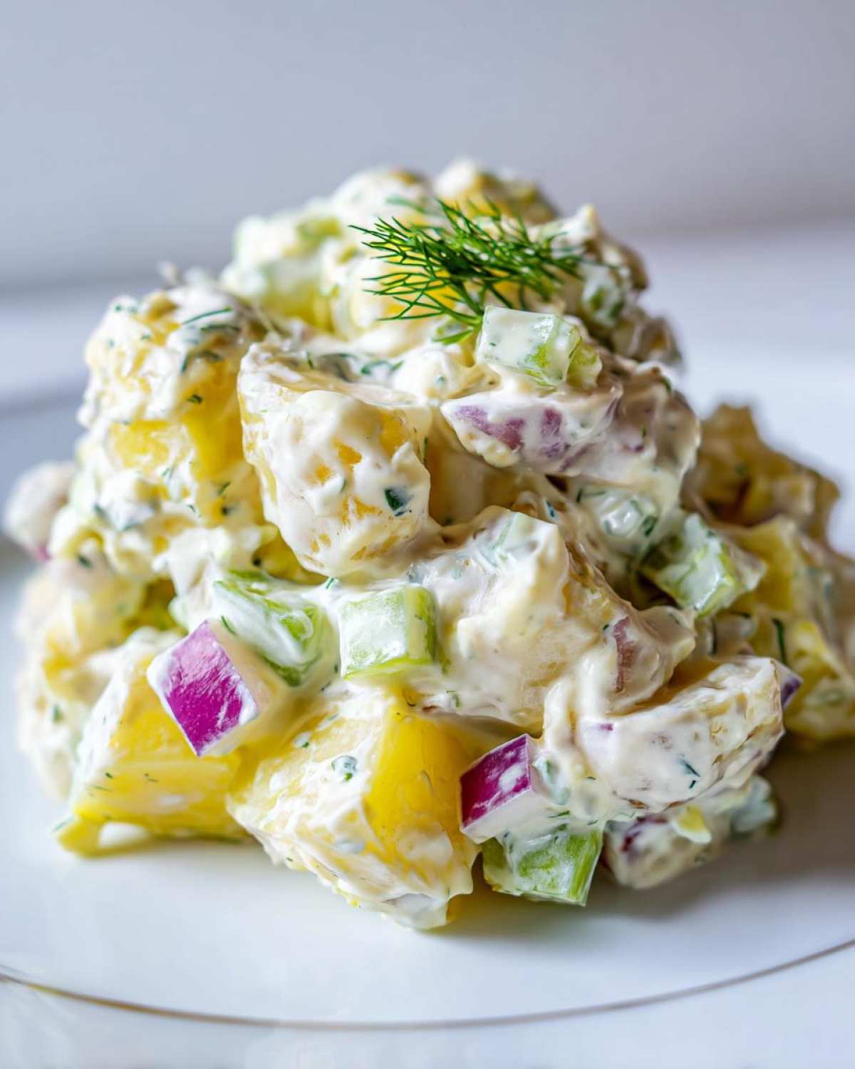 A mound of vibrant Creamy Dill Potato Salad featuring yellow potatoes, red onion, celery, and a fresh dill sprig garnish.