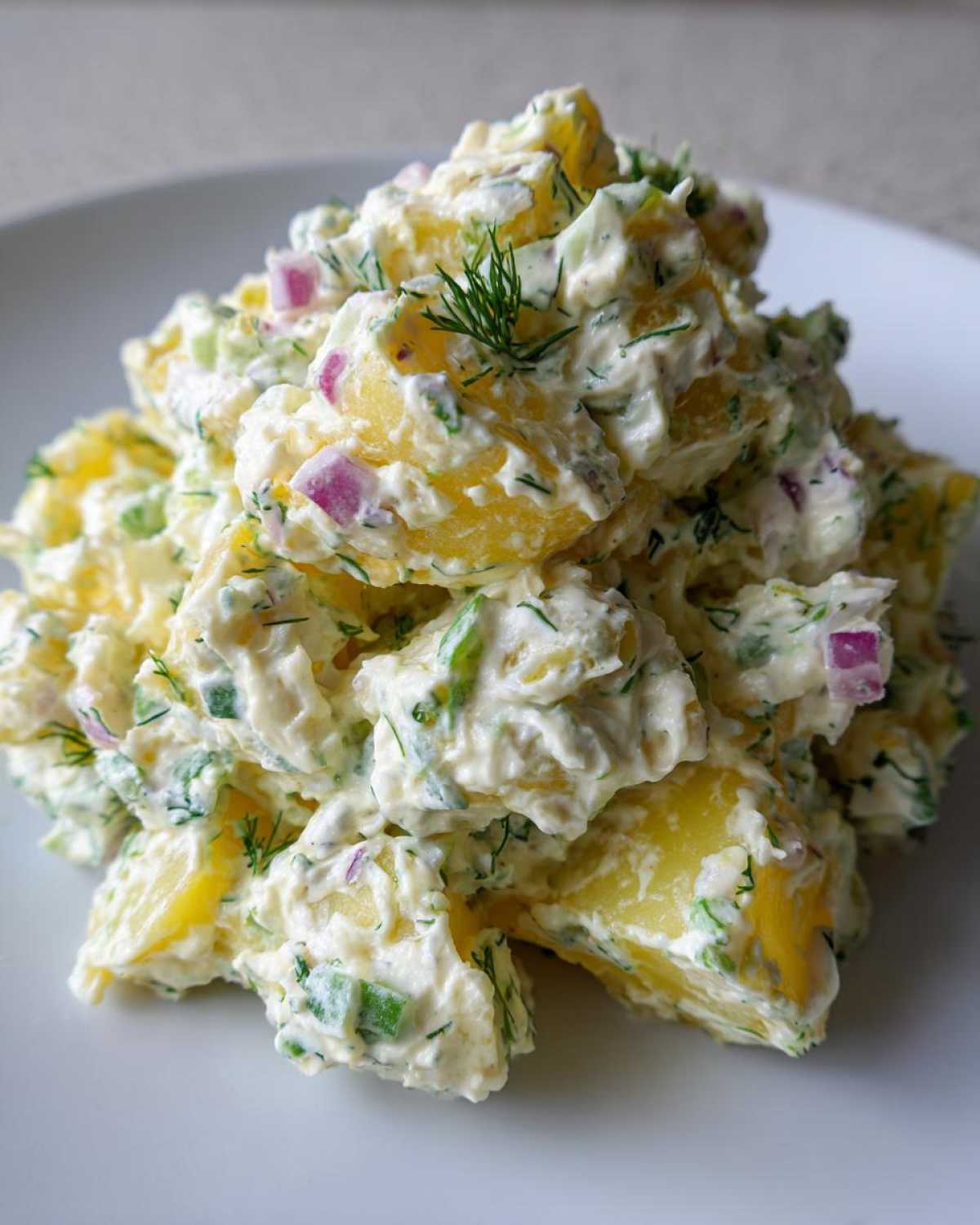 A mound of rich, creamy dill potato salad featuring yellow potatoes, red onion, and fresh dill.