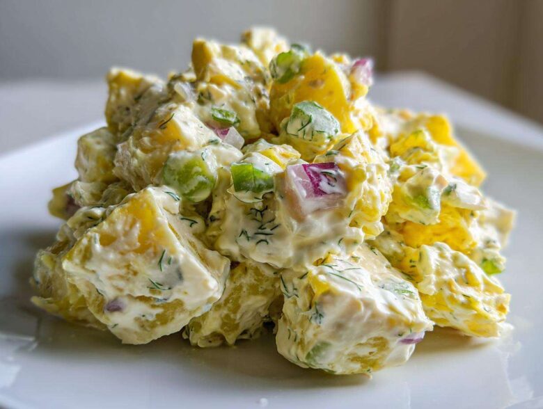 A close-up shot of a mound of Creamy Dill Potato Salad featuring yellow potatoes, red onion, green celery, and fresh dill.