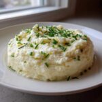 A perfectly molded serving of Creamy Garlic Mashed Cauliflower topped generously with fresh, chopped green chives.