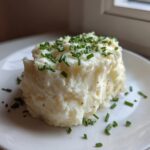 A serving of fluffy Creamy Garlic Mashed Cauliflower topped generously with fresh, chopped green chives on a white plate.