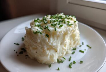 A serving of fluffy Creamy Garlic Mashed Cauliflower topped generously with fresh, chopped green chives on a white plate.