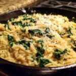 Close-up of creamy garlic parmesan orzo with spinach topped with grated cheese in a cast iron skillet.