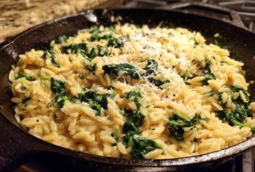 Close-up of creamy garlic parmesan orzo with spinach topped with grated cheese in a cast iron skillet.
