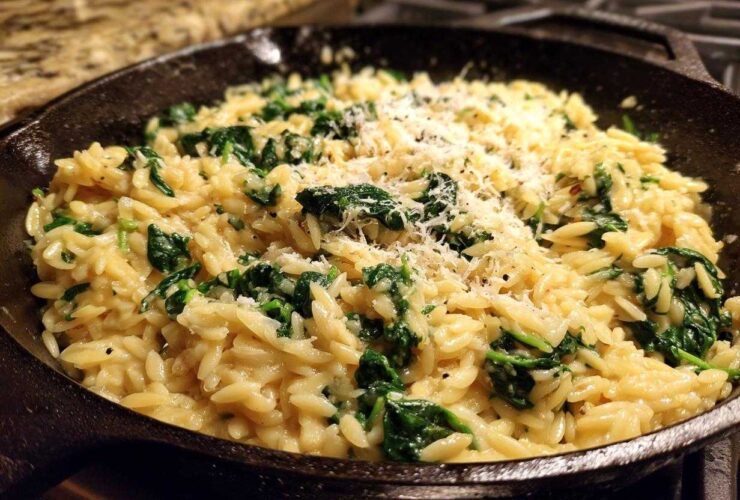 Close-up of creamy garlic parmesan orzo with spinach topped with grated cheese in a cast iron skillet.