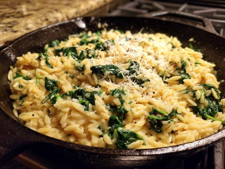 Close-up of creamy garlic parmesan orzo with spinach topped with grated cheese in a cast iron skillet.