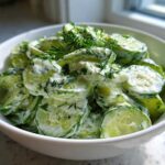 A white bowl filled with slices of Creamy German Cucumber Salad coated in a white dressing and topped with fresh dill.