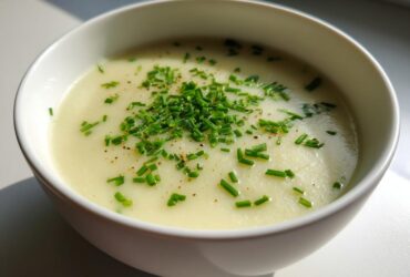 Close-up of a white bowl filled with smooth Creamy Potato Leek Soup, topped with fresh chopped chives and pepper.