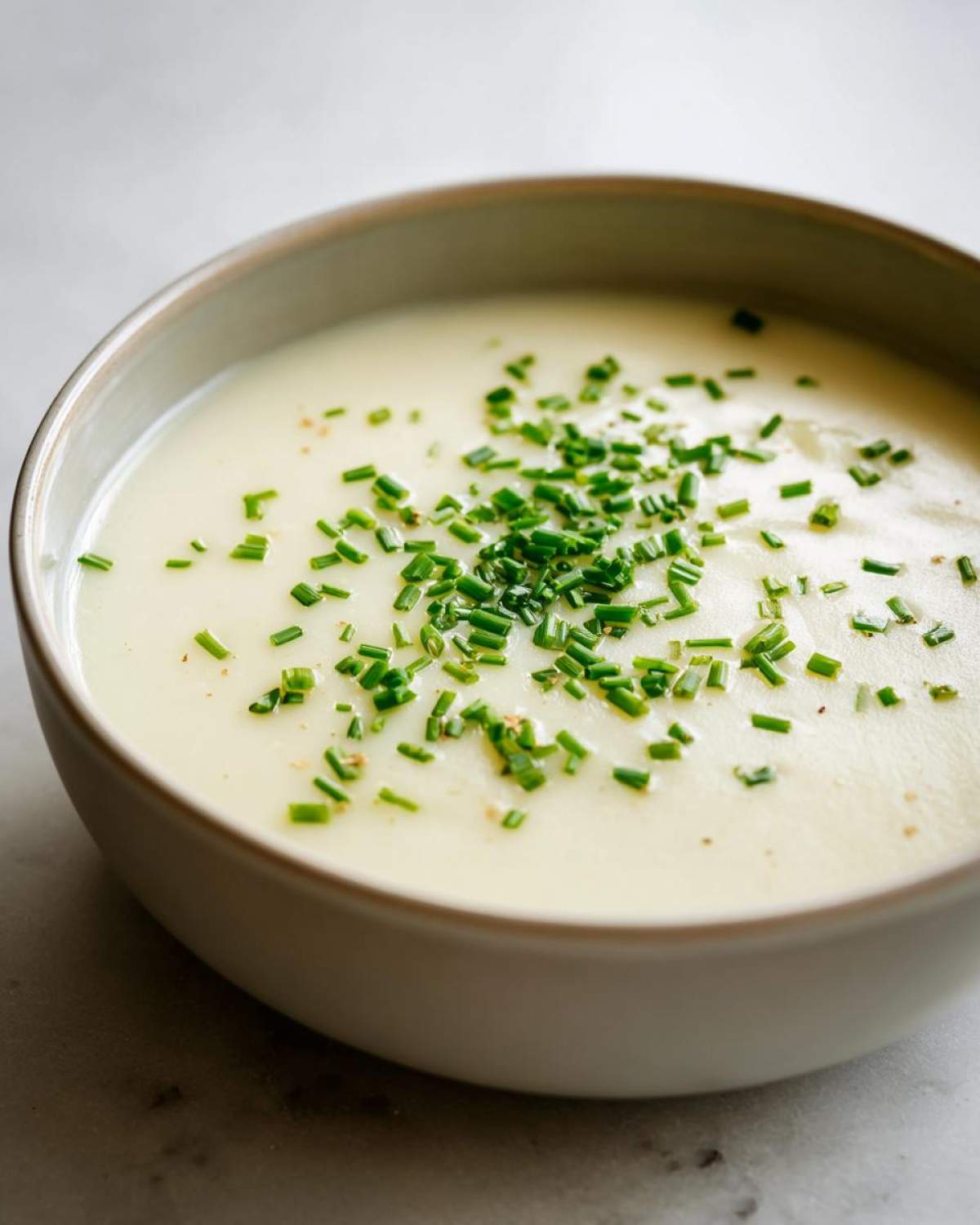 A close-up of a bowl of smooth, creamy potato leek soup garnished generously with fresh chopped chives.