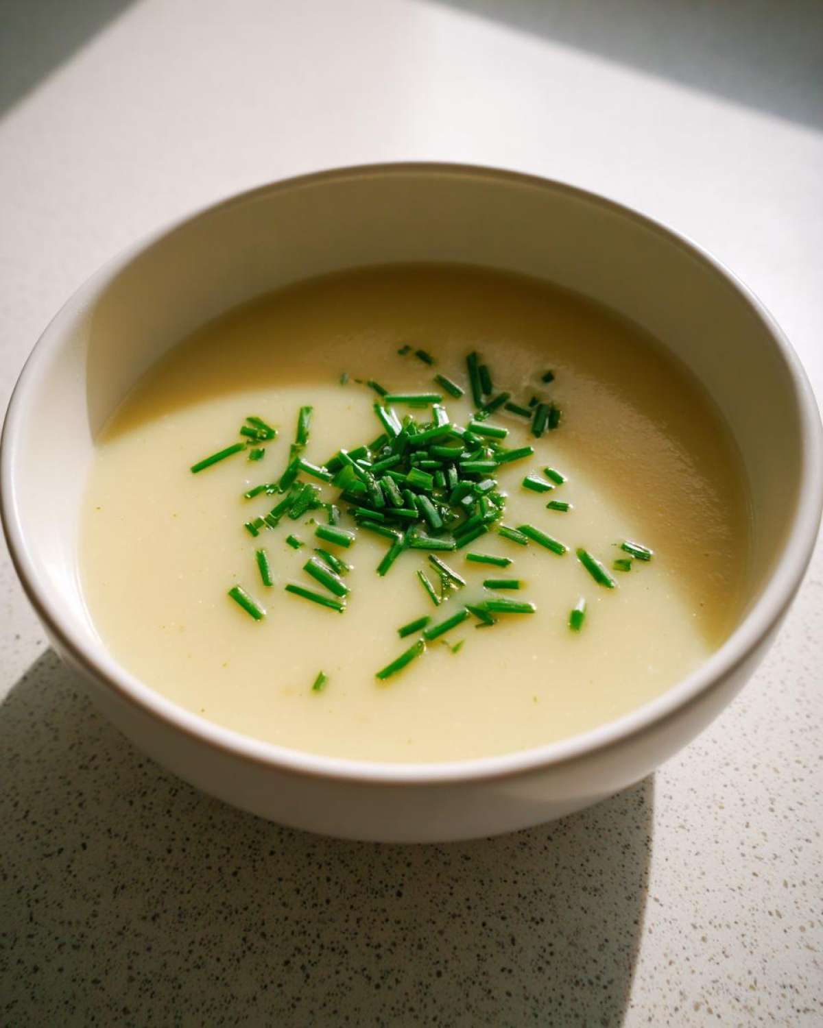 A white bowl filled with smooth, creamy potato leek soup, garnished generously with fresh chopped chives.