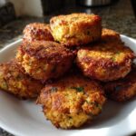 A stack of golden brown, crispy air fryer falafel patties with visible green herbs, served on a white plate.