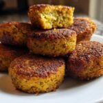 A stack of golden brown, crispy air fryer falafel on a white plate, showing the texture inside one broken piece.