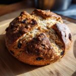 A rustic, round loaf of Easy Irish Soda Bread with Buttermilk and Raisins resting on a wooden cutting board.