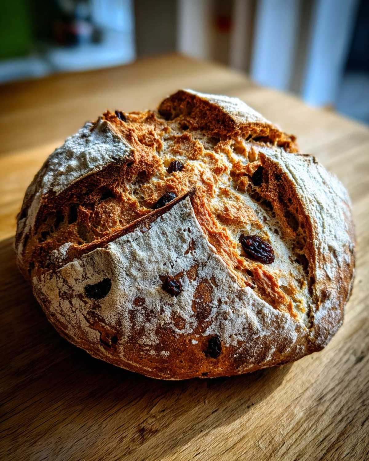 A freshly baked loaf of Easy Irish Soda Bread with Buttermilk and Raisins, dusted with flour.