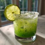 A vibrant green Fresh Jalapeño Lime Margarita served in a rocks glass with a thick salt rim and a backlit lime wheel garnish.