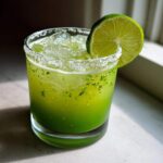 A bright green Fresh Jalapeño Lime Margarita served on the rocks with a salt rim and lime wheel garnish.