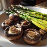 Close-up of freshly roasted Garlic Butter Roasted Asparagus and mushrooms steaming on a white plate.