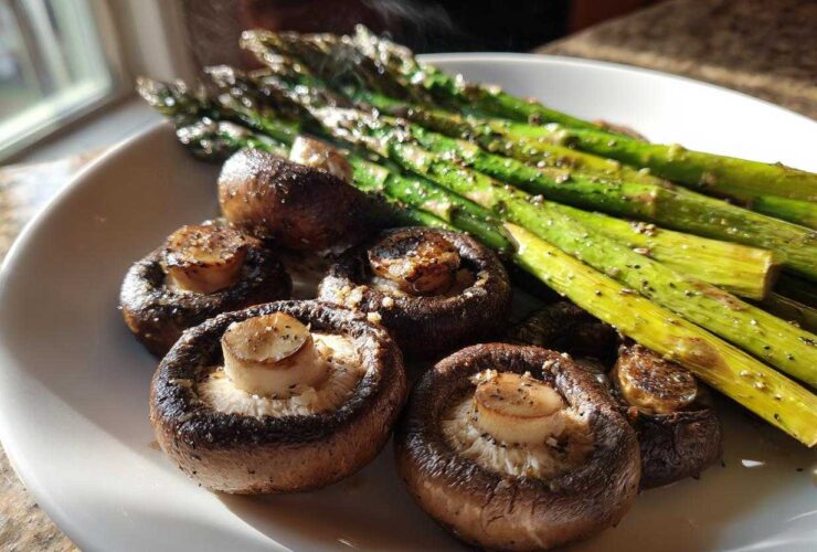 Close-up of freshly roasted Garlic Butter Roasted Asparagus and mushrooms steaming on a white plate.