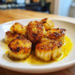 Close-up of seared Garlic Butter Scallops with Lemon resting in a pool of buttery sauce on a white plate.