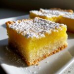 A close-up of a square of bright yellow Gluten-Free Lemon Bars with Shortbread Crust, dusted heavily with powdered sugar.