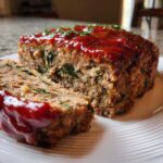 Close-up of a slice of Healthy Turkey Spinach Meatloaf topped with a shiny red glaze and fresh parsley.
