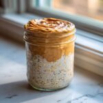 A glass jar filled with High-Protein Peanut Butter Overnight Oats, topped with swirled peanut butter.