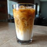 Close-up of an Iced Brown Sugar Oatmilk Latte showing beautiful swirls of coffee and oat milk over ice.