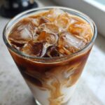 Close-up of an Iced Brown Sugar Oatmilk Latte showing rich swirls of coffee mixing with white oatmilk over ice.