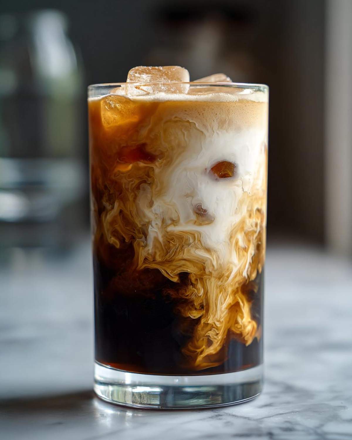 Close-up of an Iced Brown Sugar Oatmilk Latte showing rich brown syrup swirling into white oatmilk and dark espresso over ice cubes.