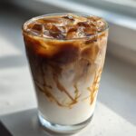 A tall glass filled with a layered Iced Caramel Macchiato, showing milk, espresso, and caramel drizzle over ice.