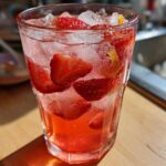 Close-up of a tall glass filled with Iced Strawberry Lemon Tea, ice, and fresh strawberry slices.