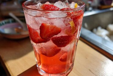 Close-up of a tall glass filled with Iced Strawberry Lemon Tea, ice, and fresh strawberry slices.