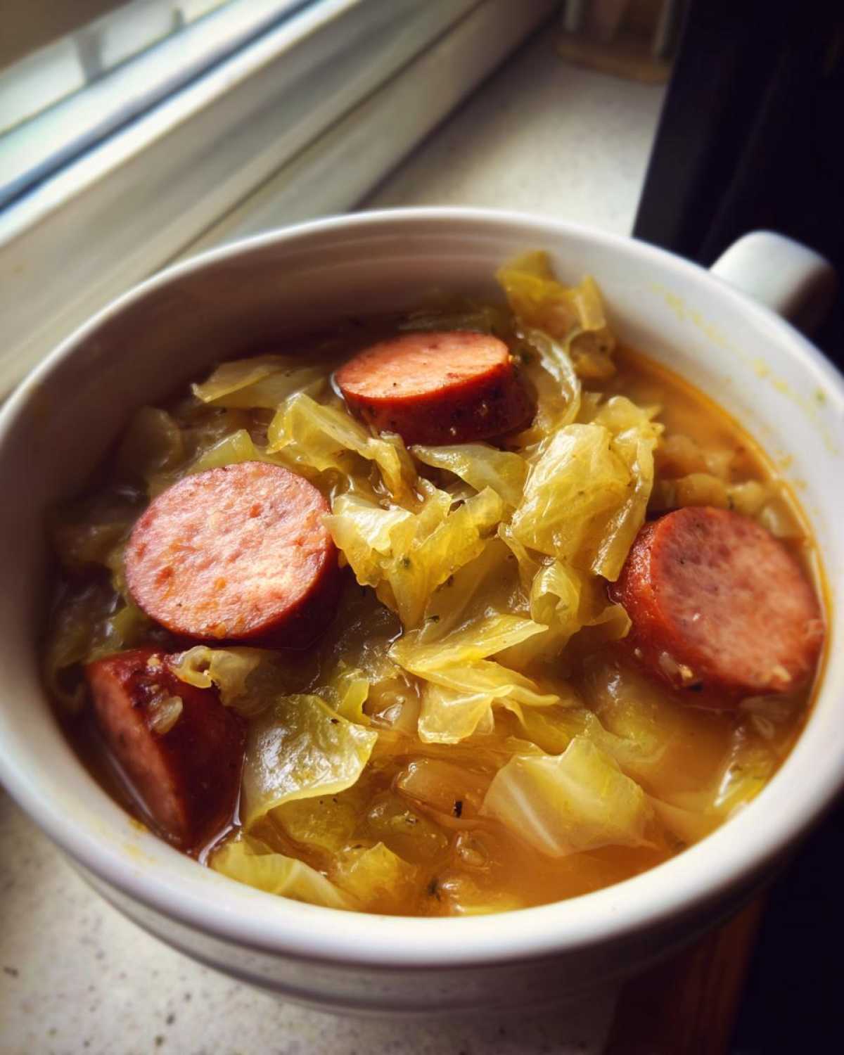 Close-up of a white bowl filled with Instant Pot Cabbage and Sausage Soup, featuring sliced sausage and tender cabbage.