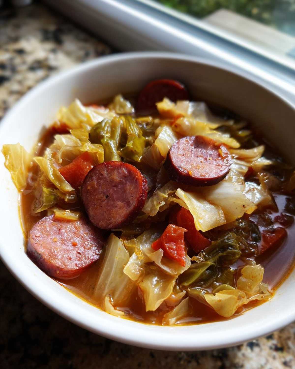 Close-up of a white bowl filled with Instant Pot Cabbage and Sausage Soup, featuring thick sausage slices and tender cabbage.