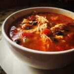 Close-up of a steaming bowl of Instant Pot Chicken Tortilla Soup with shredded chicken, black beans, and tomatoes.