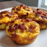 Four golden-brown Keto Bacon and Egg Muffins topped with crispy bacon pieces, served on a white plate.
