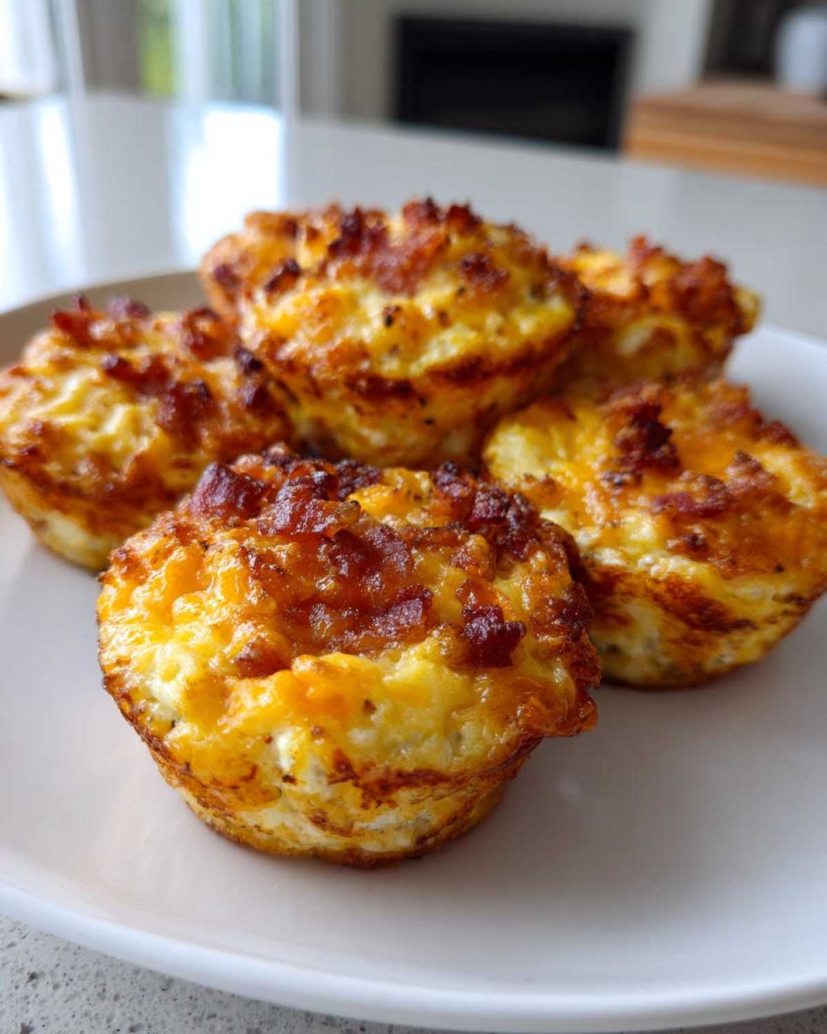 A close-up of five golden-brown Keto Bacon and Egg Muffins served on a white plate.