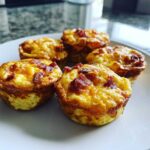Five golden brown Keto Bacon and Egg Muffins topped with crispy bacon bits served on a white plate.