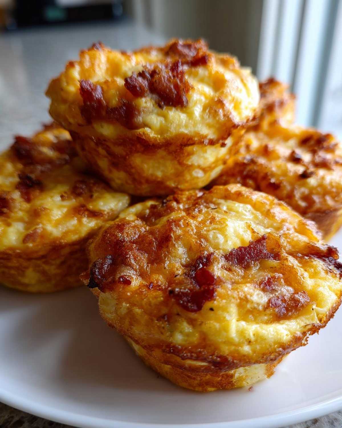 A close-up stack of golden-brown Keto Bacon and Egg Muffins showing crispy bacon bits on top.