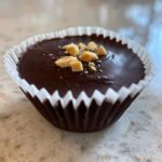 Close-up of a single Keto Chocolate Peanut Butter Fat Bomb in a white paper liner, topped with chopped peanut butter chips.
