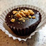 Close-up of one Keto Chocolate Peanut Butter Fat Bomb topped with crushed peanuts in a white paper liner.