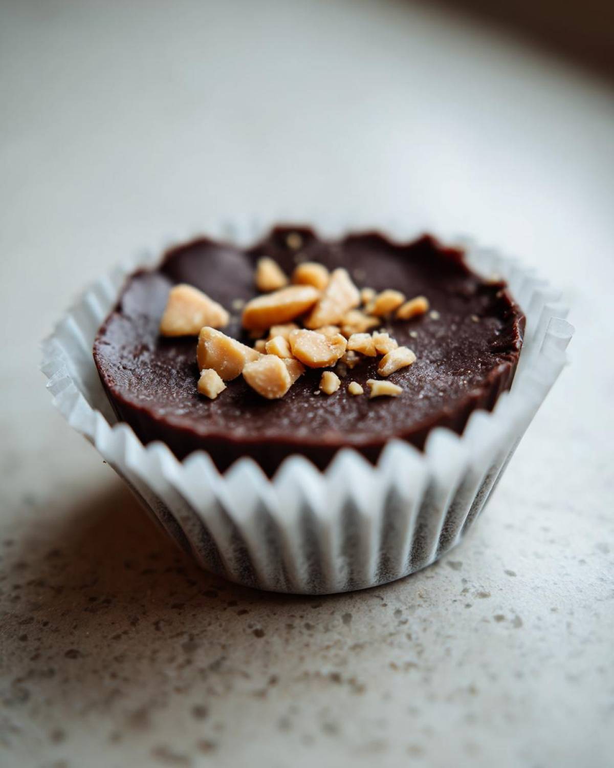 Close-up of one Keto Chocolate Peanut Butter Fat Bomb in a white paper liner, topped with chopped peanuts.
