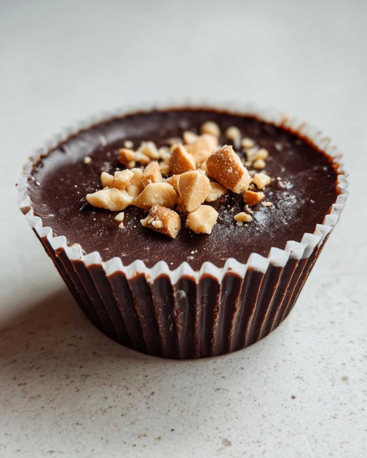 A single, rich, dark chocolate Keto Chocolate Peanut Butter Fat Bomb topped with chopped peanuts.