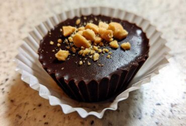 Close-up of one Keto Chocolate Peanut Butter Fat Bomb topped with crushed peanuts in a white paper liner.