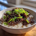 A white bowl filled with white rice topped with saucy Korean Ground Beef Bulgogi Bowls and green onions.
