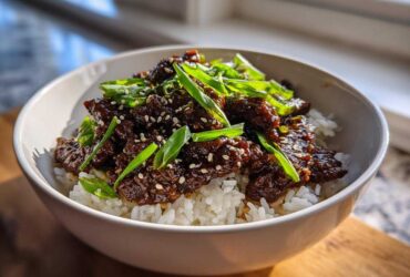 A white bowl filled with white rice topped with saucy Korean Ground Beef Bulgogi Bowls and green onions.