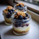 Three individual Lemon Blueberry Cheesecake Jars layered with graham cracker crust, lemon curd, cream cheese filling, blueberries, and crumble.
