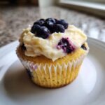 A single, moist Lemon Blueberry Cupcake topped with thick cream cheese frosting and fresh blueberries.